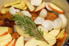 pork shoulder in pot with apple slices, onion, and a rosemary sprig