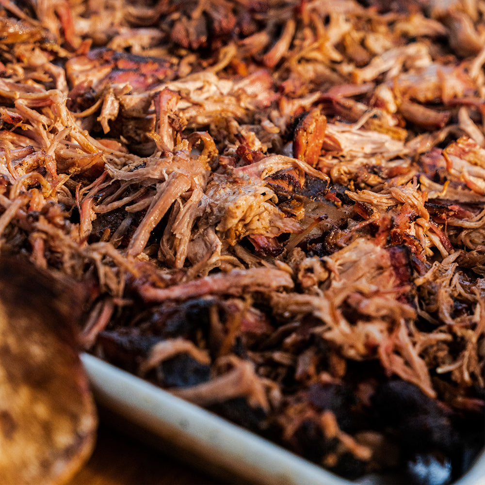 Close-up of pulled pork, with a wooden spoon edge visible in the foreground and a baking pan rim at the bottom.