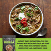 A bowl of prepared chili verde with shredded meat, green onions, cilantro, a dollop of sour cream, and sliced red chile on a wooden table, alongside a package of Fire Smoke Spiced Chili Chilt Verde and a text panel describing the flavor and ingredients.