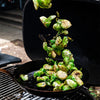 Charred Brussels sprouts falling into a black cast iron skillet on a grill grate