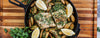 A cast iron skillet filled with cooked fish, roasted potatoes, and lemon slices, presented on a wooden cutting board with parsley.