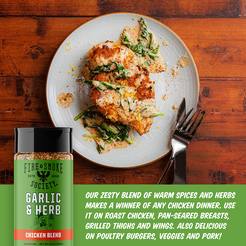 A bottle of Fire & Smoke Society Garlic & Herb Chicken Blend seasoning is shown next to a plated chicken and vegetable dinner on a wooden table, with promotional text at the bottom.