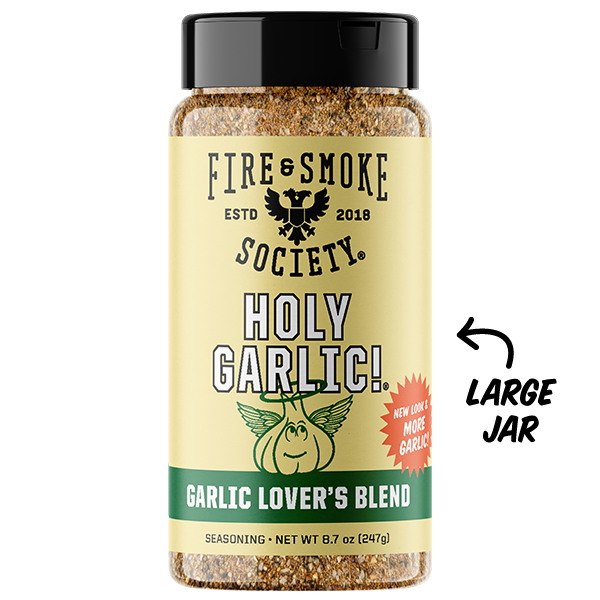 A bottle of Fire & Smoke Society Holy Garlic! seasoning on a white background, featuring a black lid, a beige label with black text and a green band, and a cartoon garlic character. A black arrow on the right points to the bottle with the text 'LARGE JAR'.