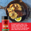 A jar of Fire Smoke Society Fat Granny's Cajun Seasoning is shown next to a cast iron skillet containing a cooked steak, shrimp, and a creamy sauce with a lemon wedge, over a blue denim background with descriptive text.