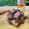 Grilled steak sandwich on a wooden cutting board with a bottle of beer in the background.