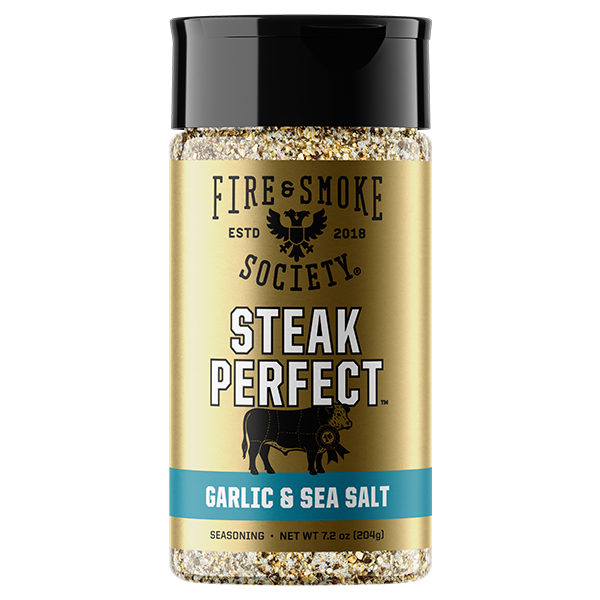 A bottle of Fire & Smoke Society Steak Perfect Garlic & Sea Salt seasoning, featuring a gold label with a black cap and a blue accent band, set against a plain white background.