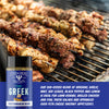 A bottle of Fire & Smoke Society Greek Mediterranean Blend seasoning is shown in the foreground against a background of grilled kebab and chicken skewers on a grill. A blue text banner at the bottom describes the seasoning blend ingredients and usage.