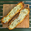 Two slices of garlic bread with cheese on a wooden cutting board.