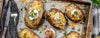 Baked potatoes with various toppings on a baking tray with utensils.