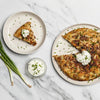 Two slices of savory pancake with sour cream and chives on a marble surface, accompanied by a small bowl of sour cream and green onions.