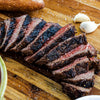 Sliced steak on a wooden cutting board with garlic and herbs
