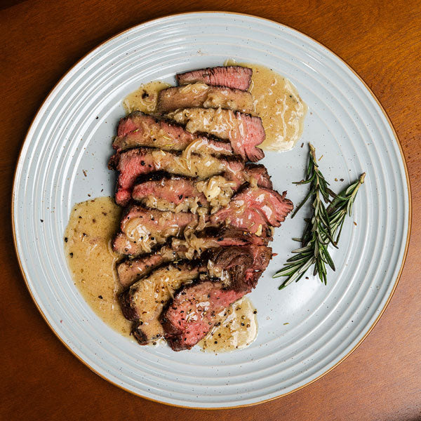 Sliced steak with creamy sauce on a white plate, garnished with rosemary.