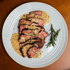 Sliced steak with creamy sauce on a white plate, garnished with rosemary.