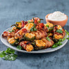 Bacon-wrapped jalapeño poppers on a plate with a side of sour cream.