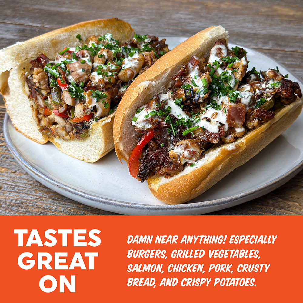 Two gourmet hoagies on a white plate, topped with chopped herbs, white sauce, and red peppers, set on a wooden table with an orange text banner at the bottom.