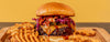 Hamburger with fries on a wooden board against a yellow background